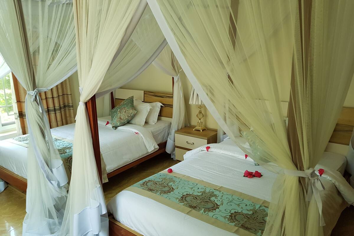 Een kamer met twee bedden, elk met een hemelbed. Er staat een nachtkastje met een lamp en een klein tafeltje naast een van de bedden.