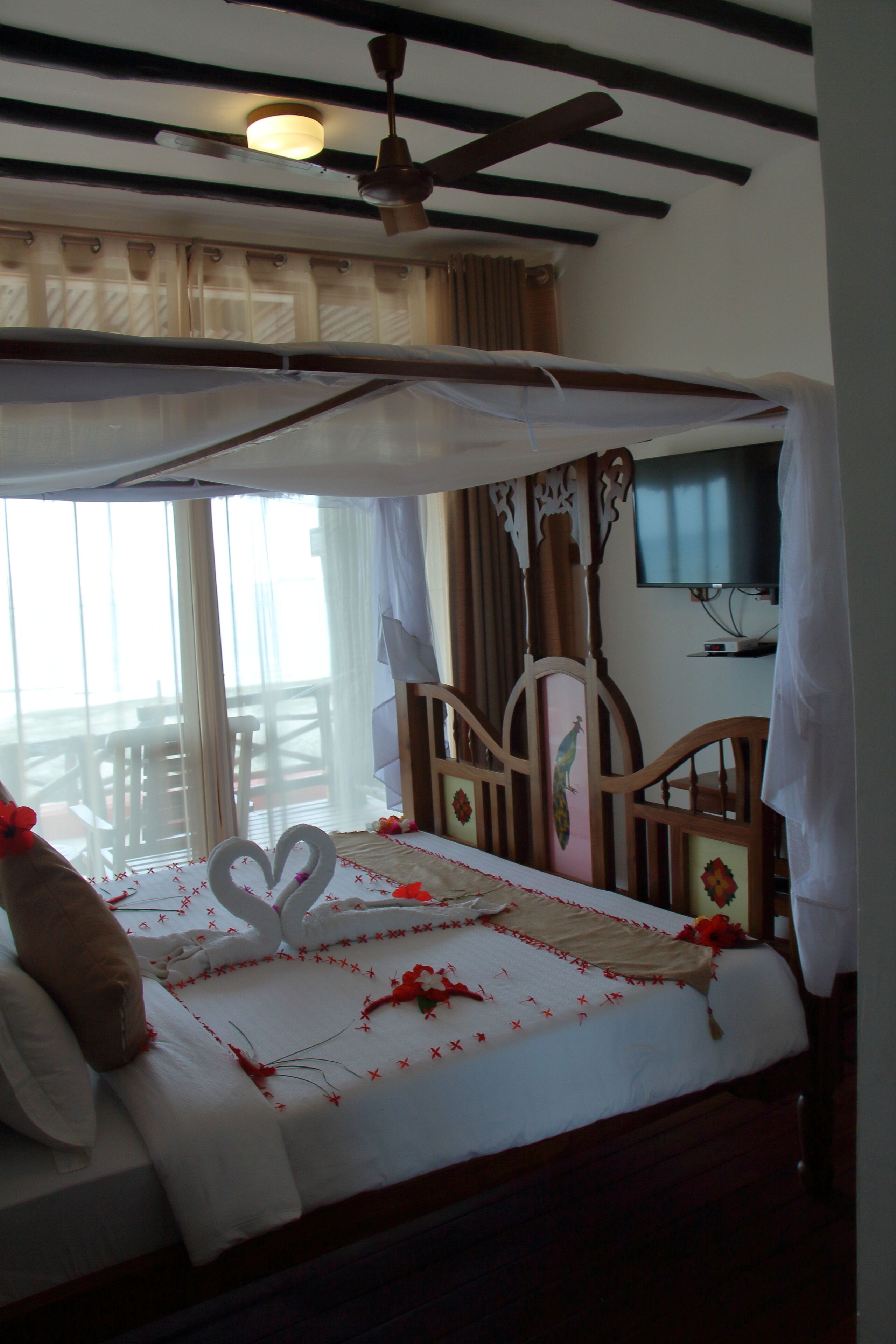 Ein Zimmer mit Bett, Deckenventilator, Fernseher und Balkon.