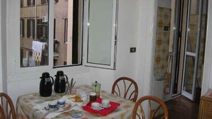 A dining area with a table set for two, a window with a view of buildings, and a sliding glass door leading to an outdoor area. - Walter Rooms (Rome)