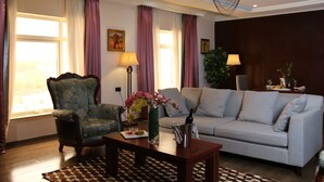 A living room with a sofa, armchair, and a coffee table with a vase and bottle. - Grand Pela Hotels & Suites (Abuja)