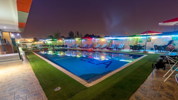 A swimming pool with 'ELLA' written on the water, surrounded by lounge chairs and umbrellas. - Grand Pela Hotels & Suites (Abuja)