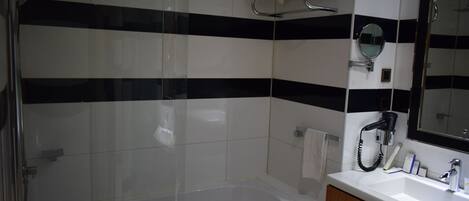 A bathroom with a glass-enclosed shower, a white bathtub, a wooden vanity with a mirror, and black and white striped tiles.
