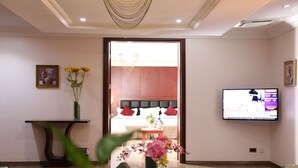 A living room with a television, a sofa, a coffee table, and a vase with flowers. - Grand Pela Hotels & Suites (Abuja)
