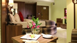 A hotel room with a bed, a sofa, a dining table with a vase of flowers, and a lamp. - Grand Pela Hotels & Suites (Abuja)