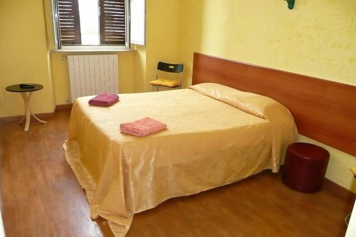A bedroom with a bed, a chair, a small table, and a radiator.