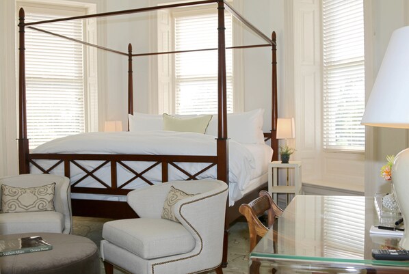 Una cama con dosel de madera, dos mesitas de noche con lámparas, una silla y una mesa de vidrio con un control remoto.