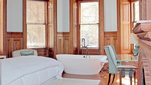 Une salle de bain spacieuse avec une grande baignoire, un lambris en bois et une table en verre accompagnée d’une chaise.