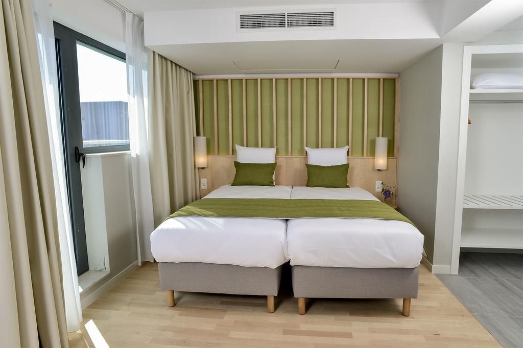 A hotel room with a double bed, two bedside tables, a wardrobe, and a sliding glass door to the balcony.