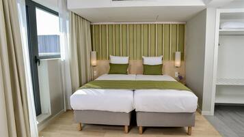 A hotel room with a double bed, two bedside tables, a wardrobe, and a sliding glass door to the balcony.