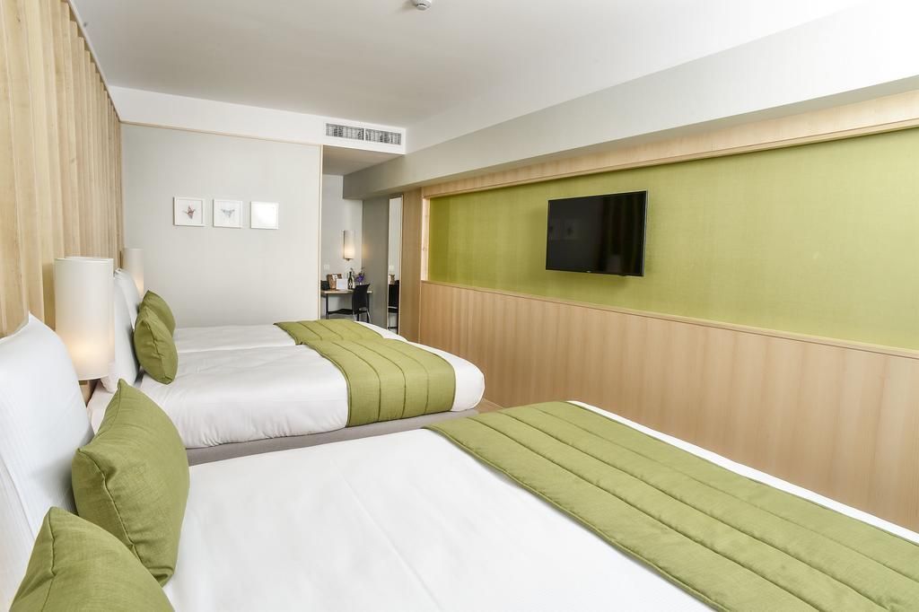 Een hotelkamer met twee bedden, een aan de muur bevestigde televisie en een klein bureau met een stoel.