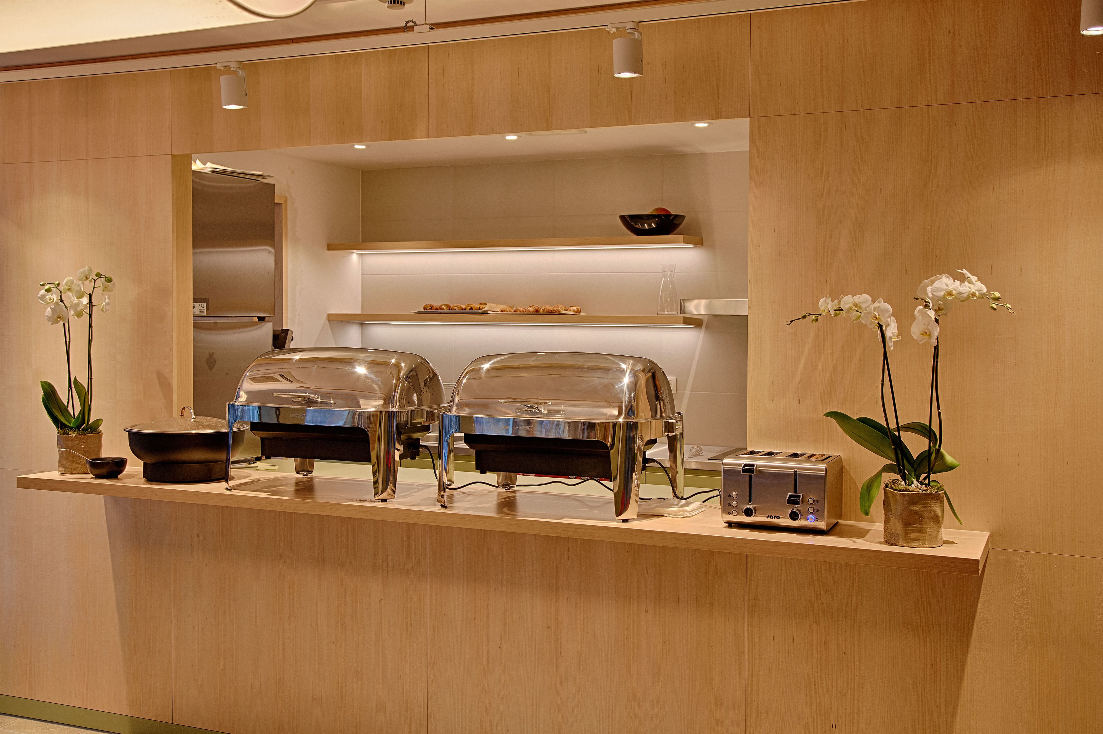 A buffet setup with two glass-covered food stations, a toaster, and potted orchids.