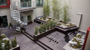 Une terrasse extérieure à plusieurs niveaux, dotée d’un plancher en bois, de jardinières intégrées agrémentées de plantes et d’un escalier en colimaçon.