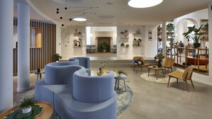 Un interior moderno con un sofá azul curvo, una mesa de centro redonda de madera y una mesita auxiliar con una planta. Se observa una chimenea al fondo y una planta grande en la esquina.