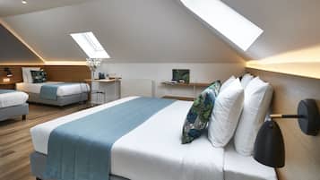 A modern bedroom with a skylight, a bed with a blue bedspread, and a desk with a chair.