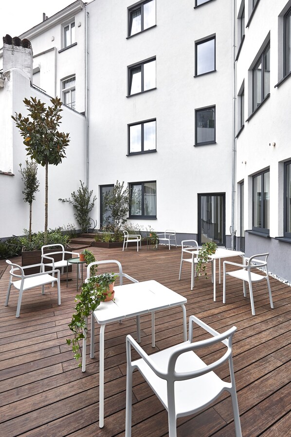 Un patio con mesas y sillas blancas, rodeado por un edificio blanco con varias ventanas.