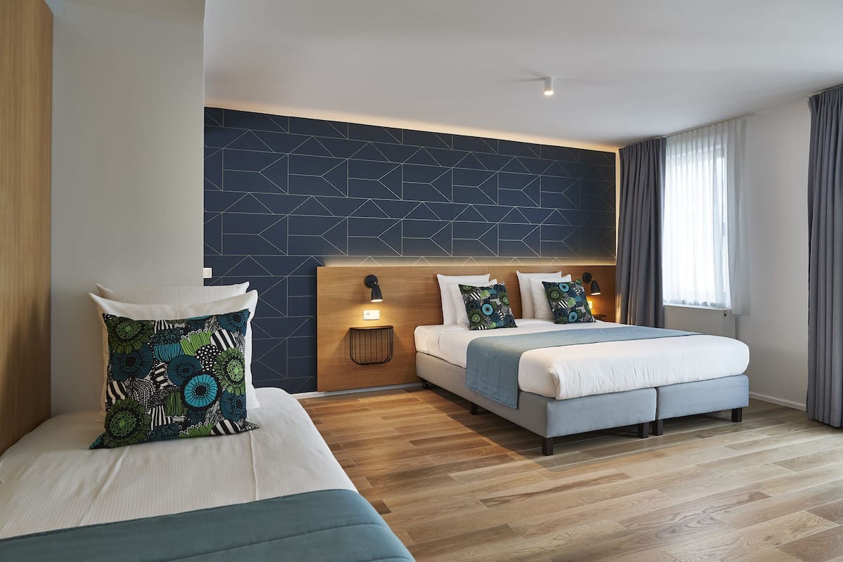 Ett modernt hotellrum med två sängar, en vägg med ett geometriskt mönster och ett trägolv.