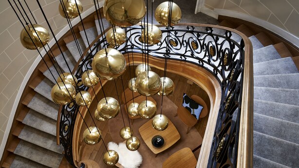 Una imponente escalera con barandales negros ornamentados y múltiples lámparas esféricas doradas.