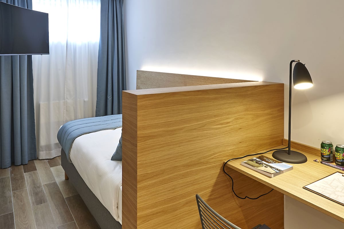 Ett hotellrum med en säng, ett skrivbord med en lampa, en stol och en tv.