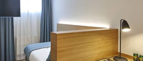 A hotel room with a bed, a desk with a lamp, a chair, and a TV.