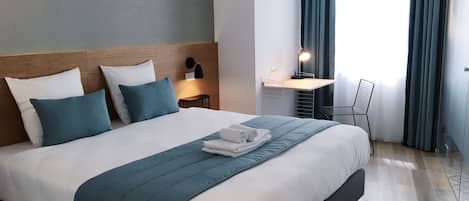 A neatly made bed with a blue and white duvet, a wooden headboard, and a bedside table with a lamp.