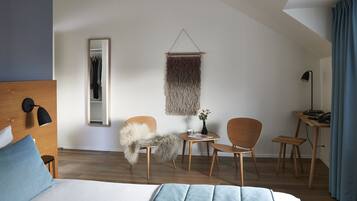 Habitación de hotel moderna con una cama grande, cabecera de madera, escritorio con silla, una mesita con un florero y un tapiz colgante.