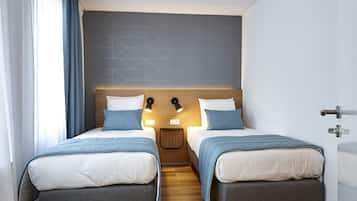 Ein modernes Hotelzimmer mit zwei Einzelbetten, Holzboden, einem Kopfteil mit geometrischen Mustern und einem Nachttisch mit Lampe.