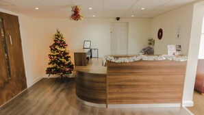 A reception area with a wooden reception desk, a Christmas tree, and a wall-mounted sign. - Primelodge Doncaster (Doncaster)