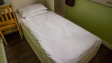 A single bed with white bedding in a room with green walls and wooden flooring.