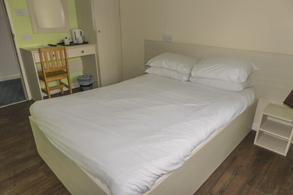 A neatly made bed with white linens, a wooden chair, a small bedside table, and a desk with a coffee maker. - Primelodge Doncaster (Doncaster)