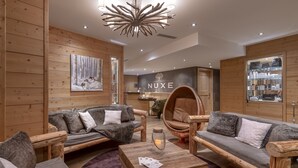 Un interior moderno con paneles de madera, un letrero de NUXE, una chimenea y un área de descanso con un sillón redondo y sofás.
