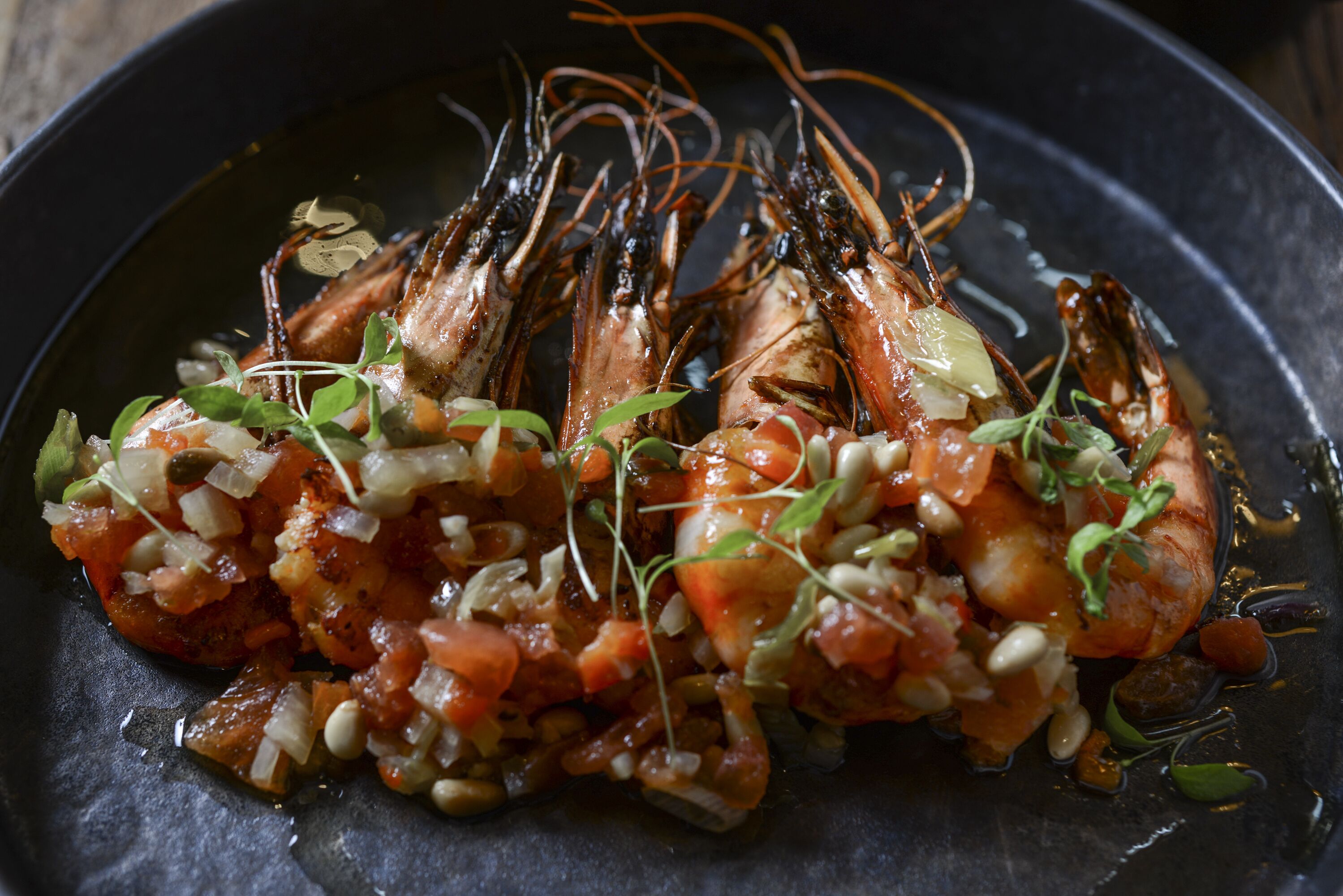 A dish of cooked shrimp with a tomato-based sauce and garnishes.