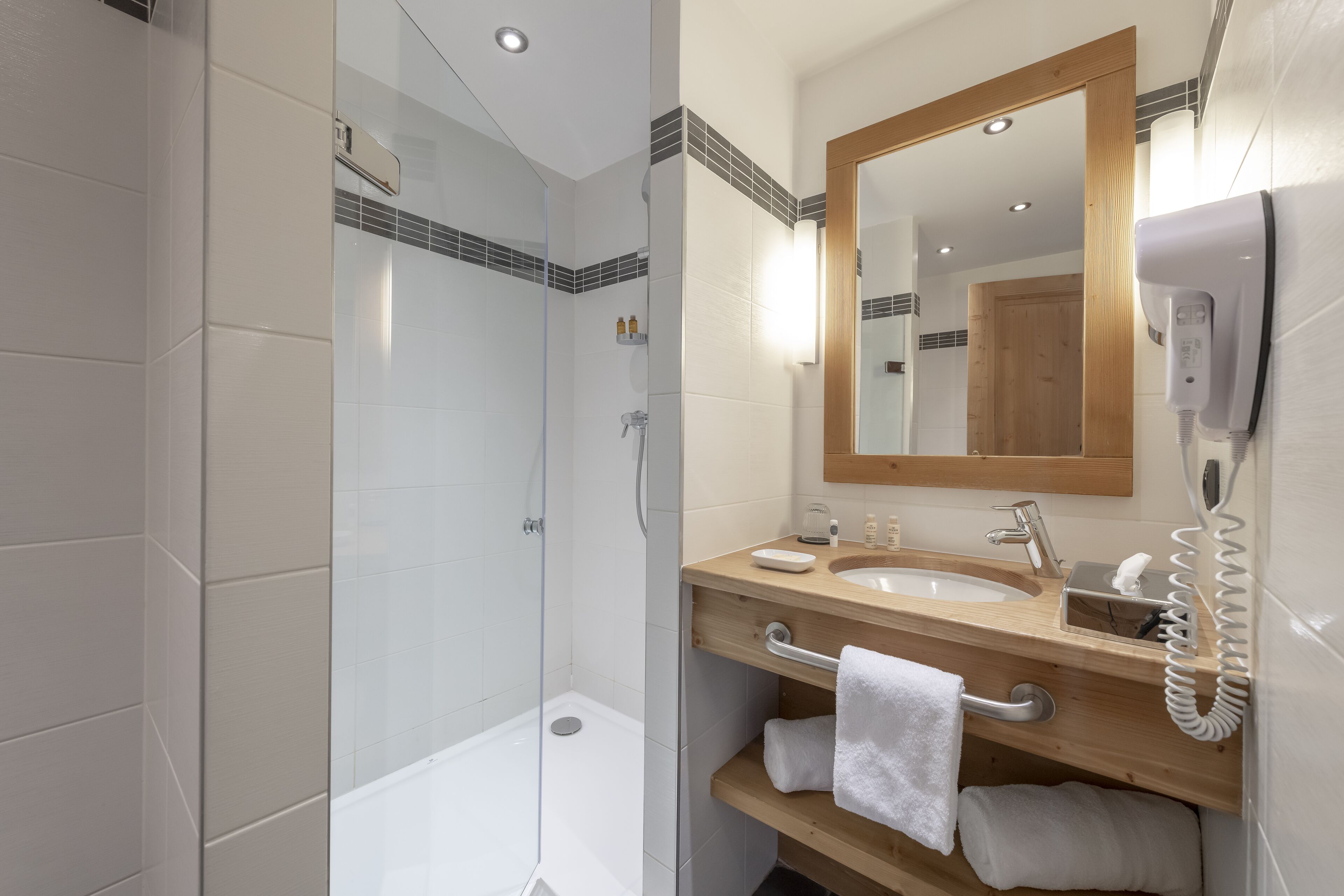 Un baño moderno con cabina de ducha de vidrio, tocador de madera con lavamanos y un espejo.
