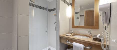 Un baño moderno con cabina de ducha de vidrio, tocador de madera con lavamanos y un espejo.