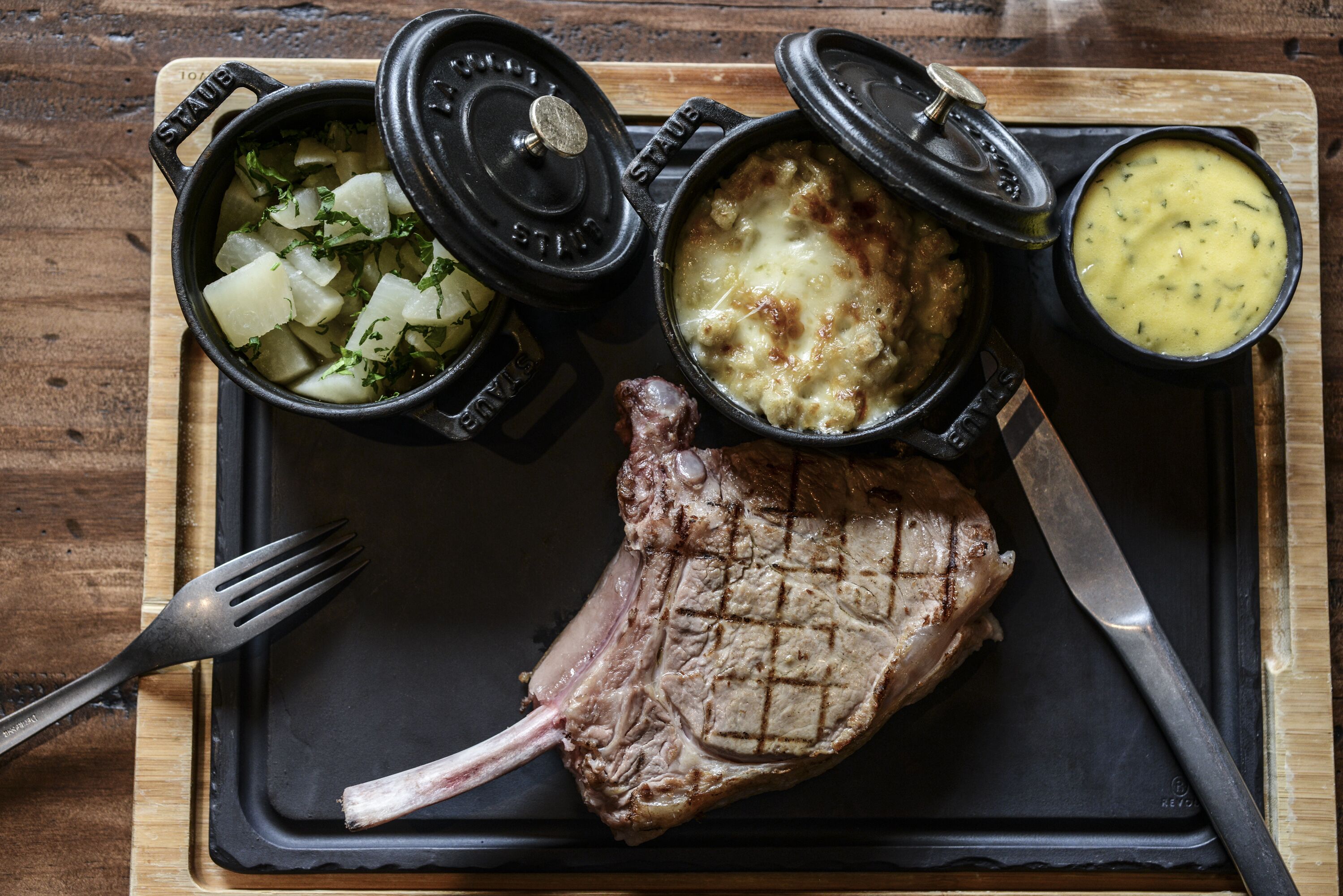 Un plato con un bistec a la parrilla, guarnición de papas en cubos y dos recipientes pequeños con salsas.