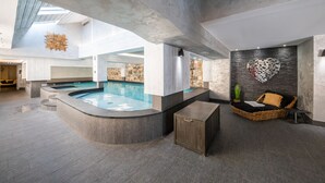 Un área de piscina interior moderna con una pared de piedra, un mosaico con forma de corazón y una silla de salón de mimbre.