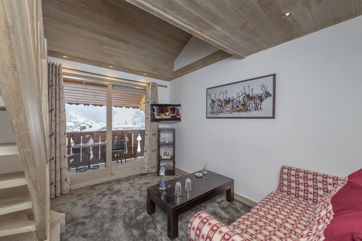 A cozy living room with a wooden ceiling, a sofa, a coffee table, and a TV.