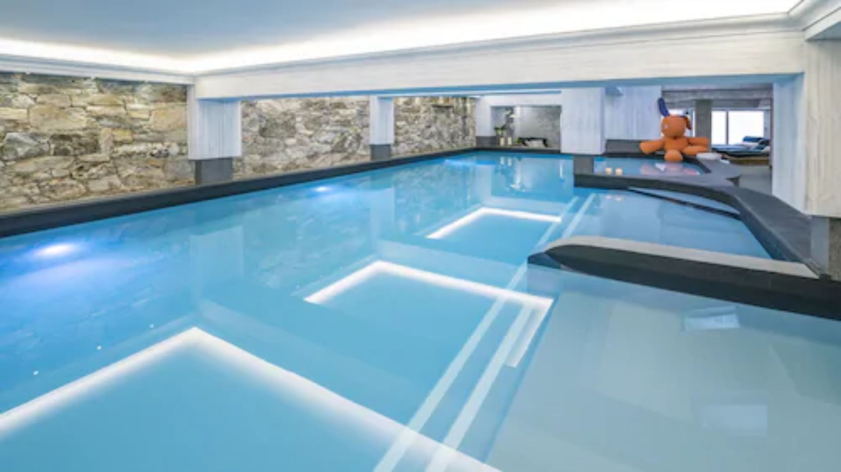 Una piscina interior moderna con paredes de piedra y agua azul cristalina.