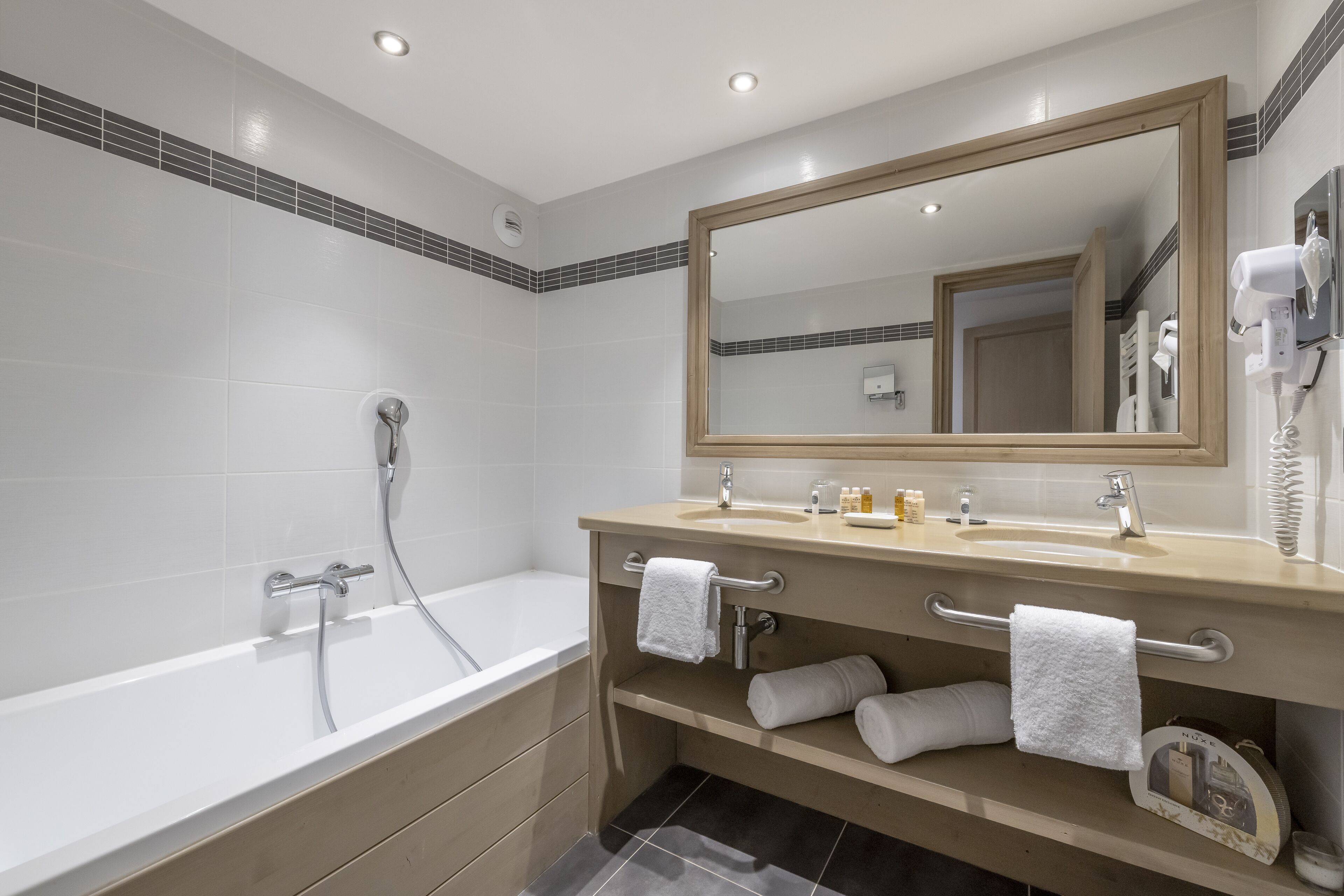 A modern bathroom with a bathtub, a vanity with a mirror, and a hairdryer.