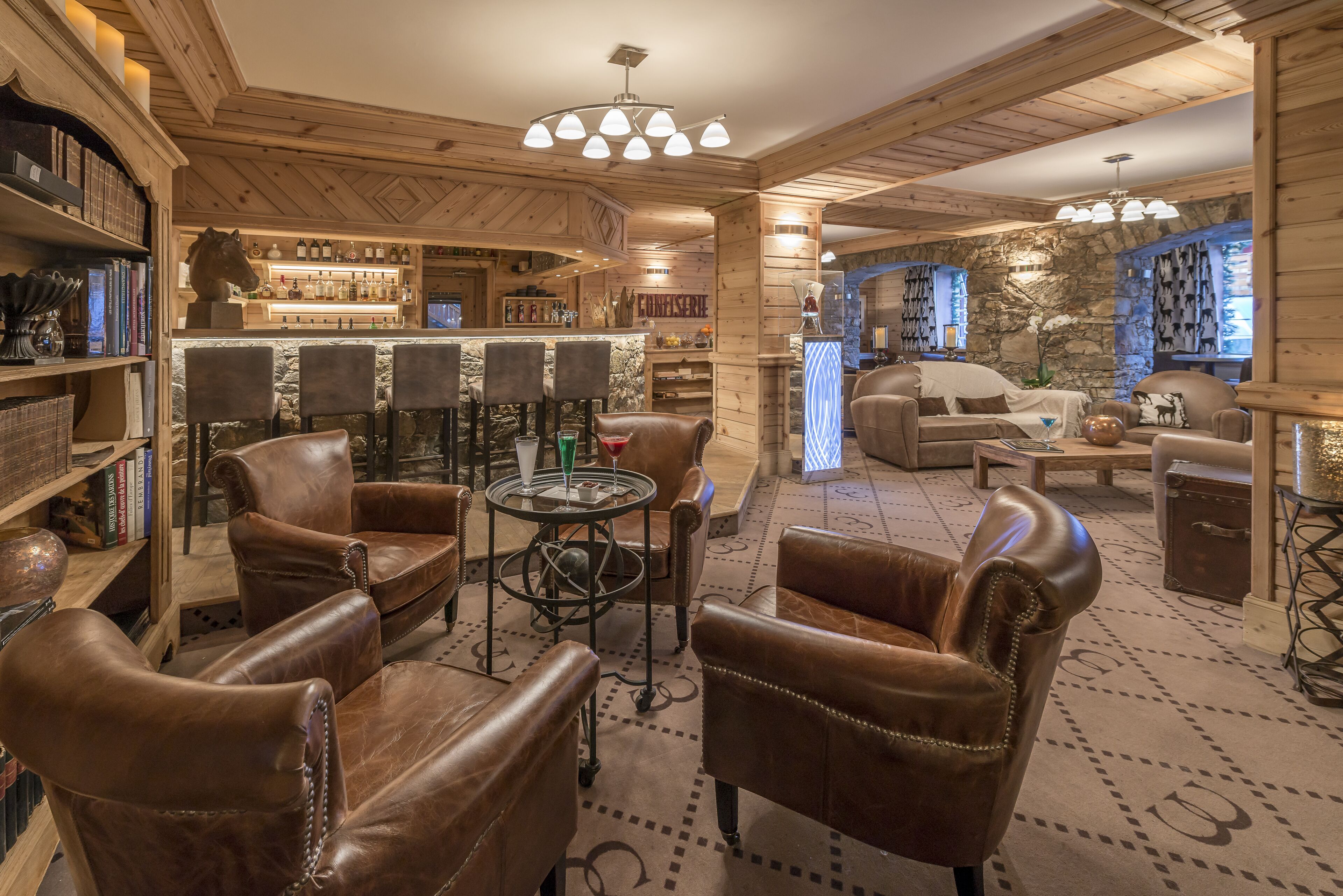 A cozy, wood-paneled room with leather chairs, a bar area, and a stone wall.