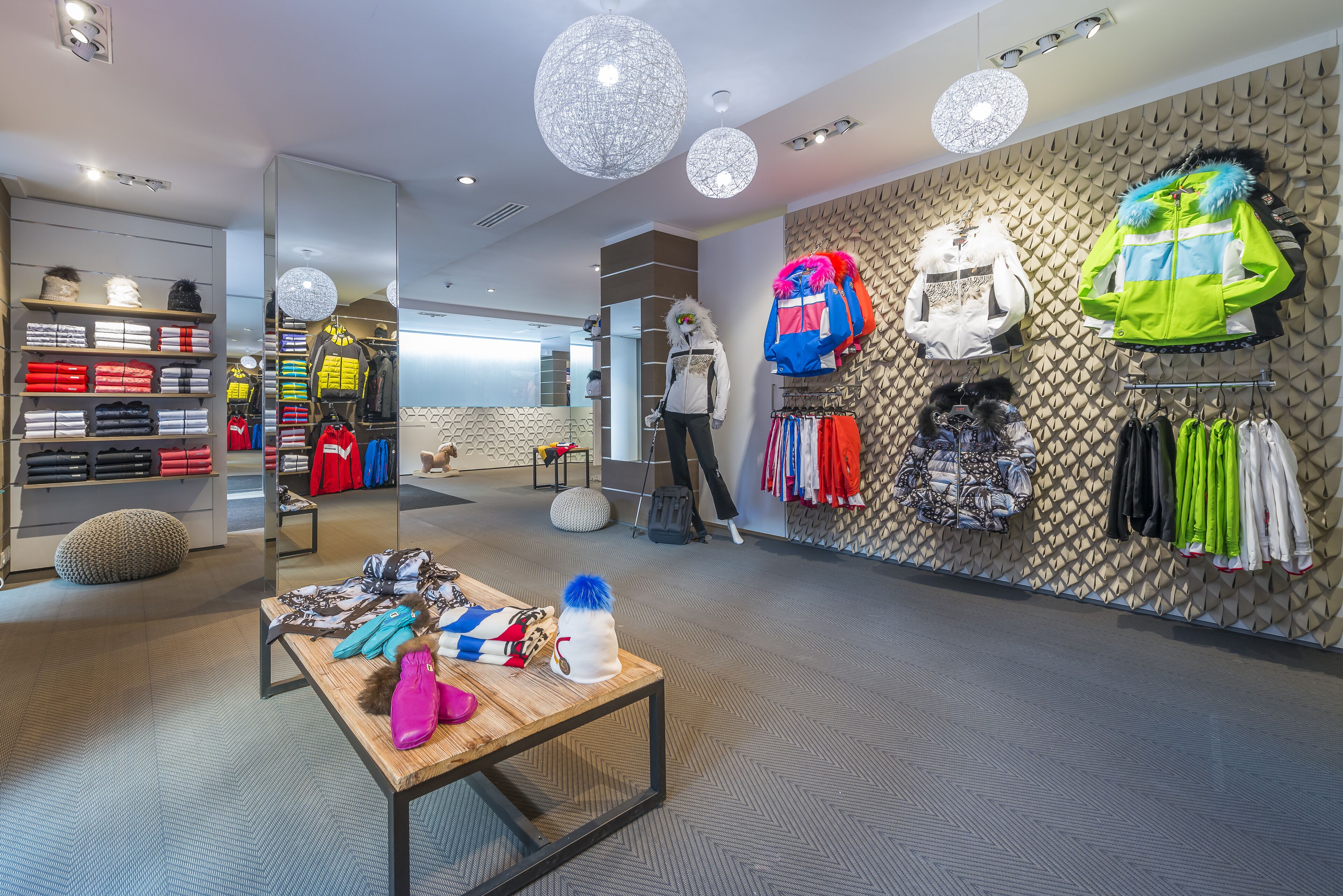 A modern retail space with clothing racks, a mirrored wall, and a wooden table with items on it.