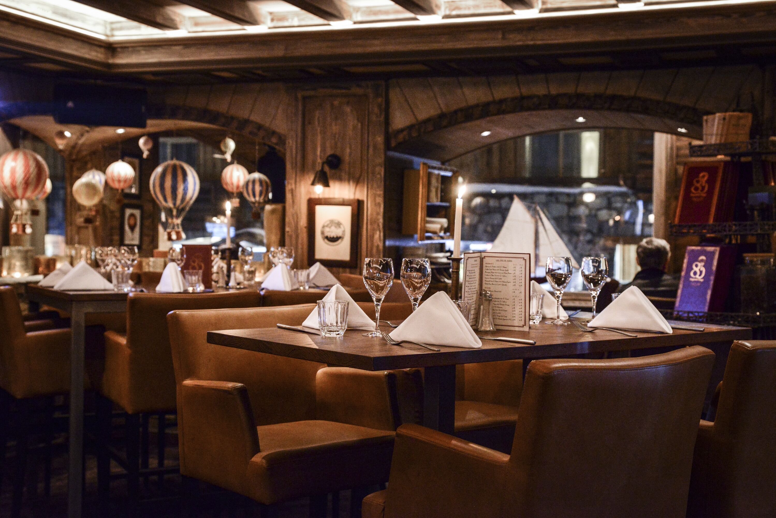 Un restaurant avec des tables et des chaises en bois, des menus et des verres à vin disposés pour le service.