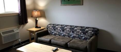 Ein Zimmer mit einer Couch, einem Tisch, einer Lampe und einem Gemälde an der Wand.
