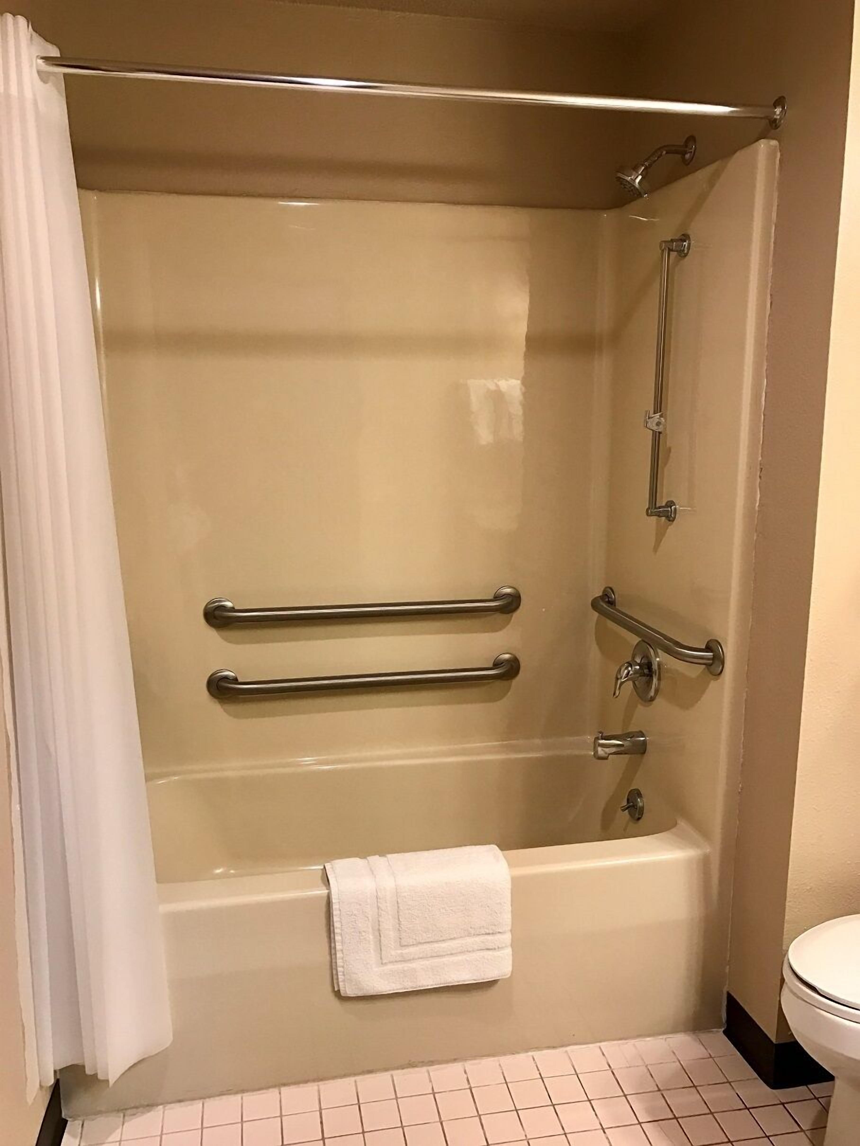 Un baño con bañera, barras de apoyo, toallero y un inodoro.