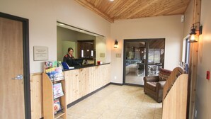 A reception area with a wooden reception desk, a counter, and a seating area with a sofa and chairs. - Woodside Dells Hotel & Suites (Wisconsin Dells)