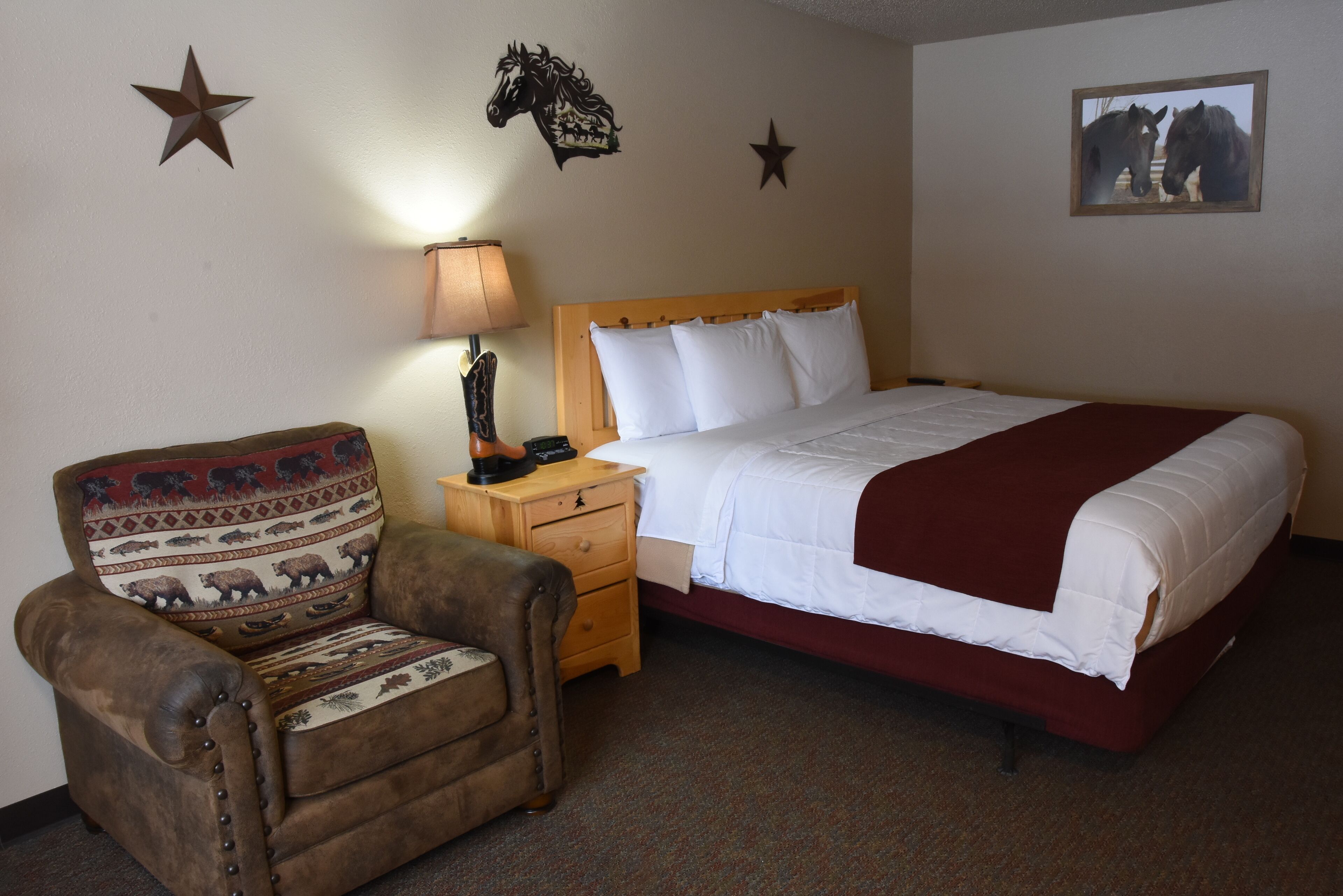 Habitación de hotel con cama, mesita de noche de madera, lámpara, silla con cojín estampado y adornos en la pared, incluyendo estrellas y un caballo.