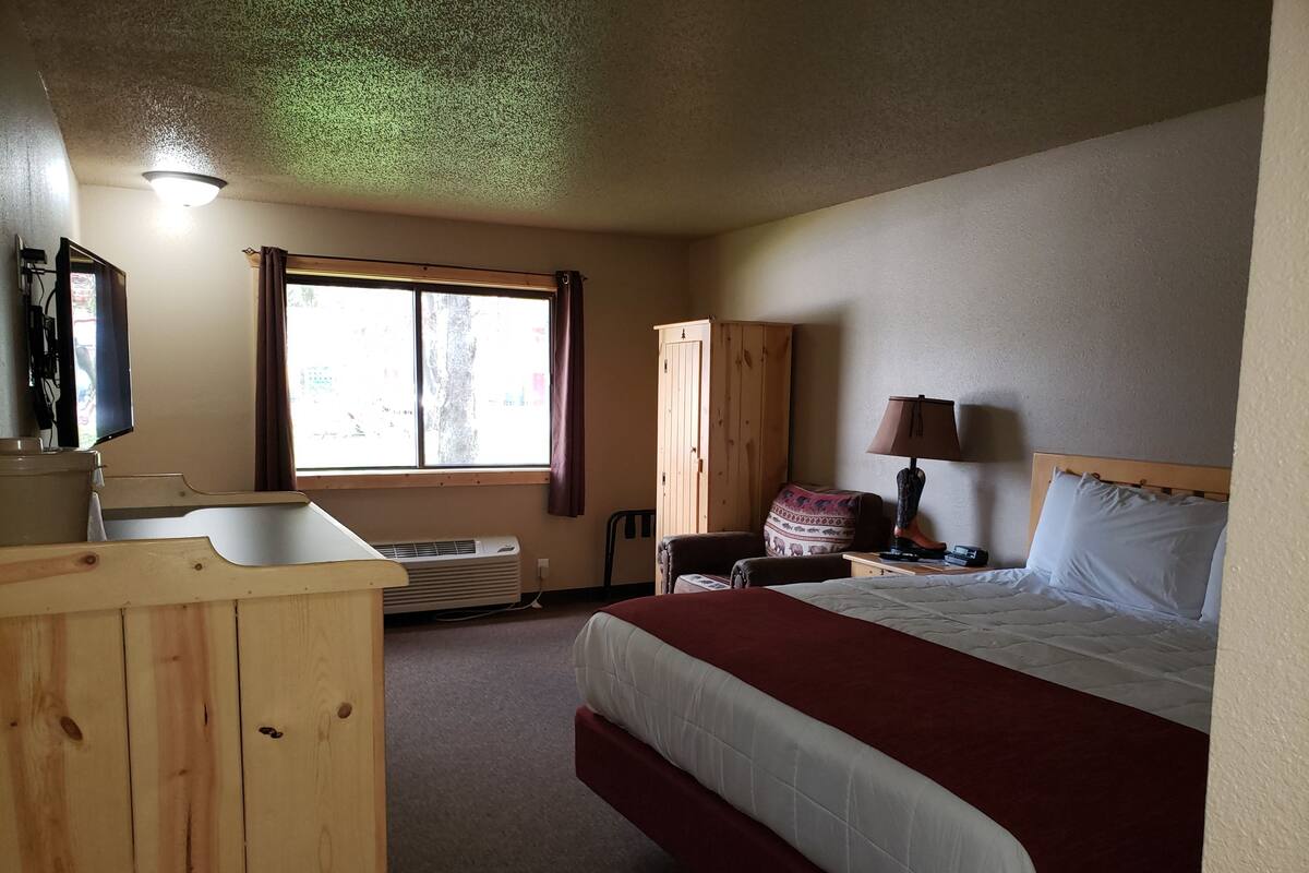 A hotel room with a bed, a wooden desk, a television, a window, and a wardrobe.