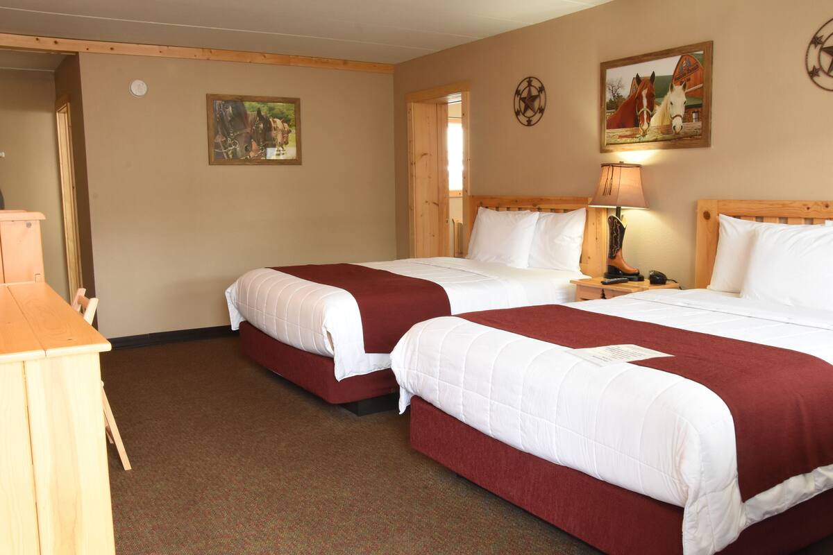 A hotel room with two beds, a wooden headboard, a nightstand with a lamp, and a painting on the wall.