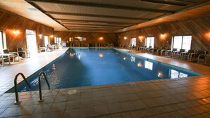 An indoor swimming pool with tiled flooring, wooden walls, and multiple lounge chairs around the perimeter. - Woodside Dells Hotel & Suites (Wisconsin Dells)