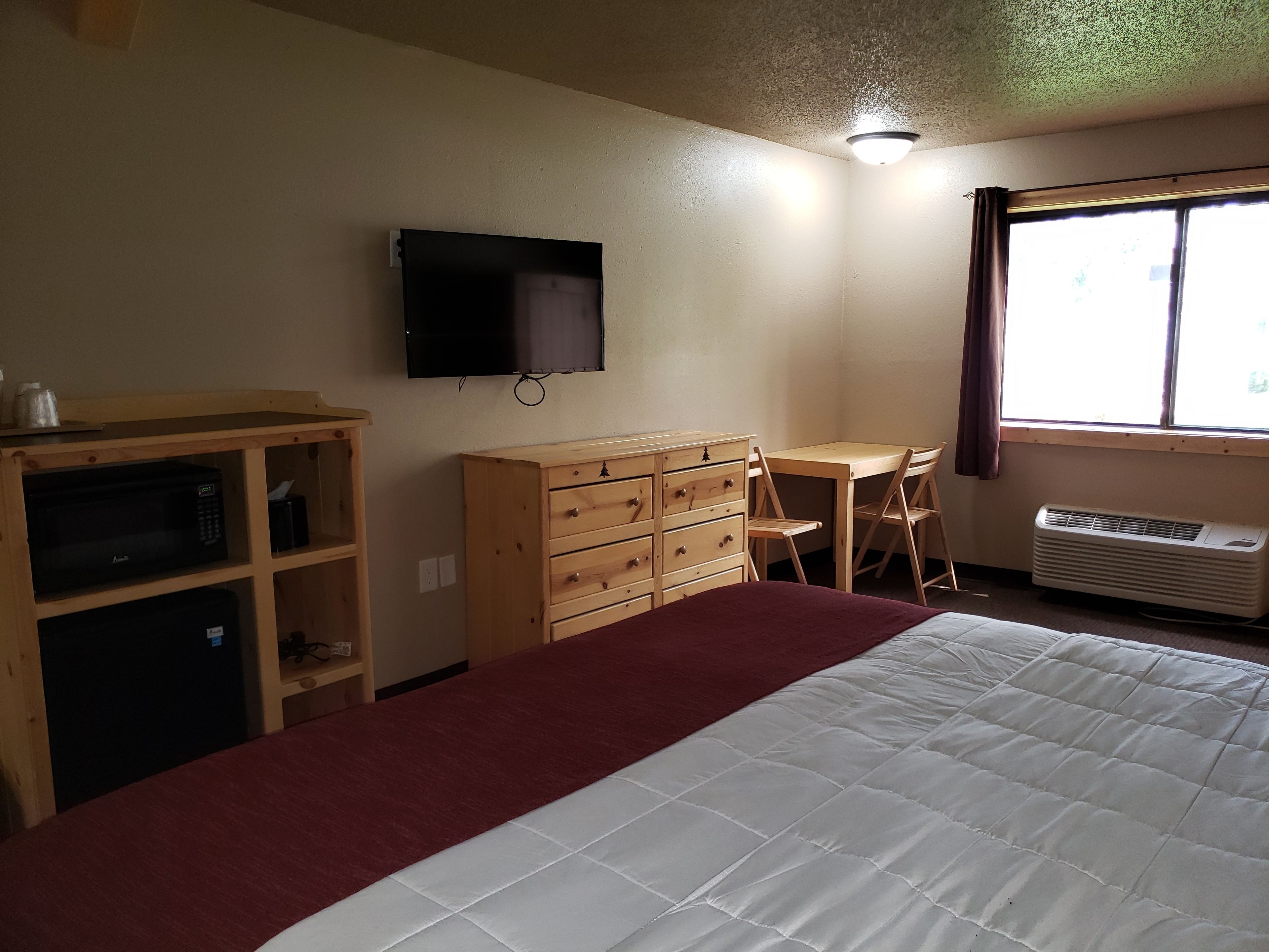 A bedroom with a bed, a desk, a dresser, a television, and a window with curtains.