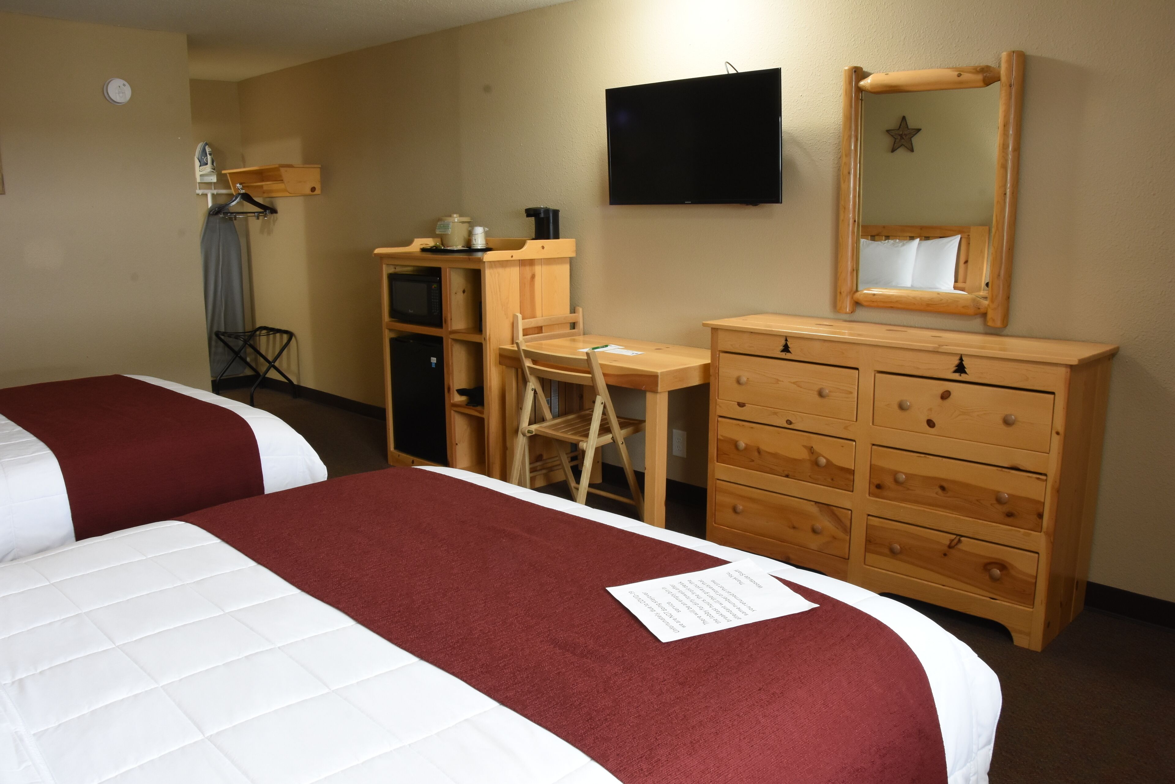 Une chambre d’hôtel avec deux lits, un bureau, une commode, une télévision et un miroir.